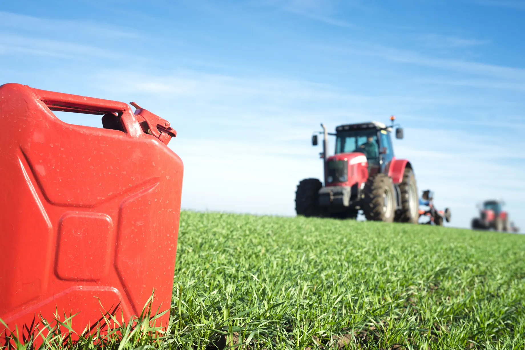 Bote rojo de combustible en campo con tractor